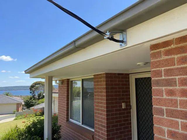 Overhead service cable and bracket on a brick home exterior with eaves in Wangi Wangi