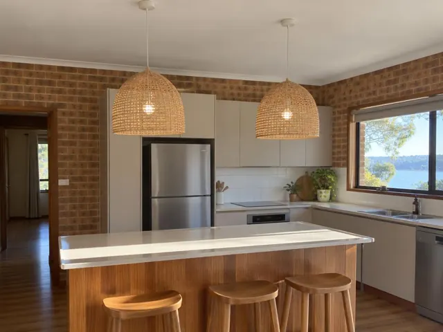 Two woven pendant lights above a kitchen island in a brick-walled home interior in Wangi Wangi